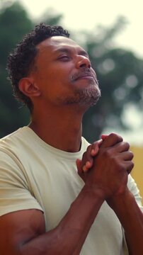 African American man clasping hands and looking upward in serene outdoor prayer and devotion