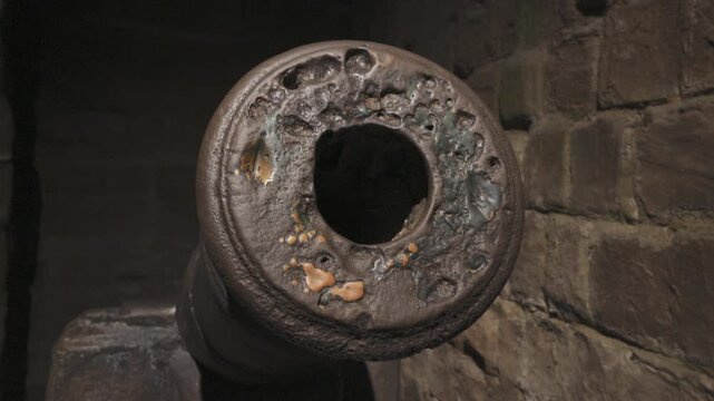 Slow orbiting rotating camera movement focusing on old historic iron cannon muzzle, weathered rust‑stained metal texture, dark brick wall background, historical military relic close‑up shot.
