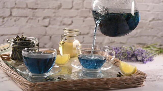 Butterfly pea flower tea is poured into a clear glass cup. Fresh lemon juice is added to the blue herbal tea, creating a natural color change from blue to purple, and stirred with a spoon.