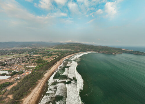Aerial view of the scenic Pacitan Beach coastline with rolling ocean waves, sandy shores, and lush green hills in Pacitan, East Java, Indonesia.