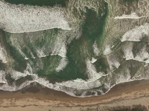 Aerial view of Pacitan Beach with powerful waves crashing onto the sandy shoreline in Pacitan, East Java, Indonesia.