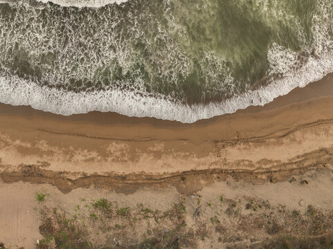 Aerial view of Pacitan Beach with white waves crashing onto the sandy shore and lush coastal vegetation in Pacitan, East Java, Indonesia.