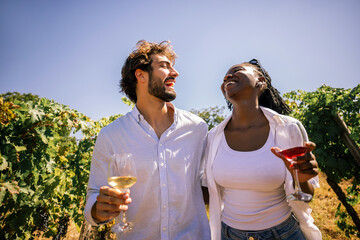 Obraz premium Couple laughing together while enjoying wine in a sunny vineyard