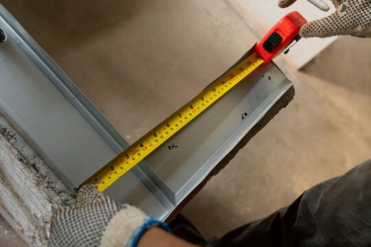 Hands wearing measuring a drywall stud with a tape measure on site