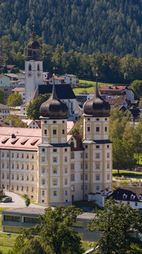 Aerial view of Stift Stams with its iconic onion-domed towers and historic architecture surrounded by the village and lush green landscape in Stams, Tirol, Austria.