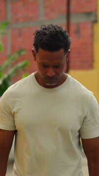 African American man walking along urban street with calm and reflective expression near yellow wall
