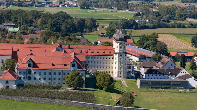 Aerial view of Stift Stams monastery with its distinctive twin-towered church, red-tiled roofs, and surrounding green fields in the alpine landscape of Stams, Tirol, Austria.