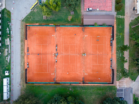 Aerial view of three clay tennis courts in a sports facility with players, surrounding grass, and pathways in Turin, Piedmont, Italy.