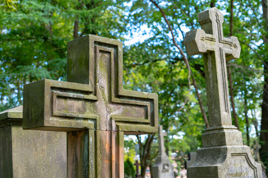Two weathered stone crosses in a historic cemetery, large carved Christian grave monuments surrounded by lush green trees and old tombstones