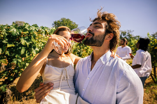 Happy couple drinking wine together among grapevines in a vineyard
