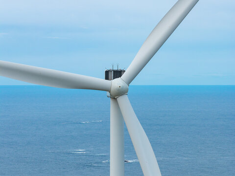 Aerial view of a wind turbine on Haramsoya with white blades rotating against the backdrop of the blue sea in Haram, More og Romsdal, Norway.