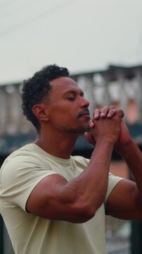 African American man standing outdoors with hands clasped near face in reverent prayer