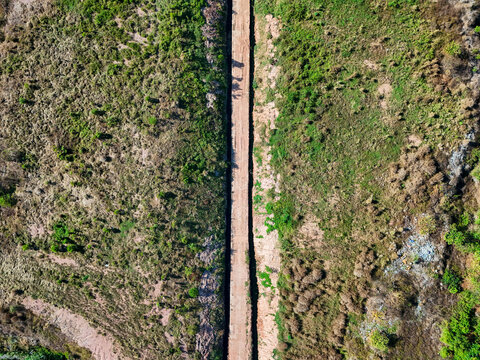 Aerial view of a straight dirt path cutting through grassy terrain in Banjarmasin City, South Kalimantan, Indonesia.