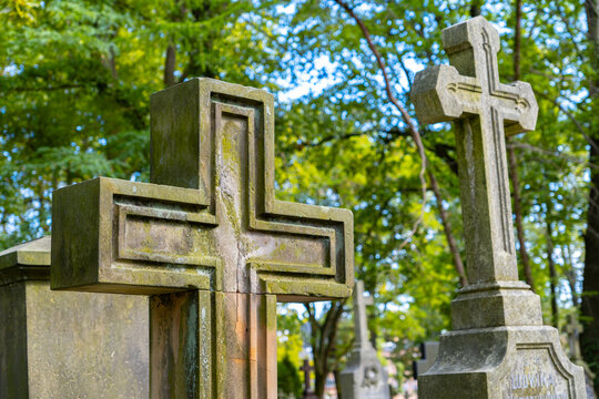 Two weathered stone crosses in a historic cemetery, large carved Christian grave monuments surrounded by lush green trees and old tombstones