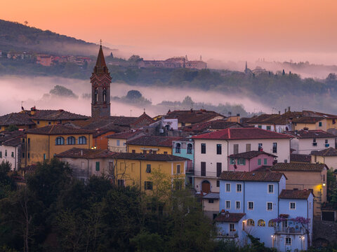Aerial view of the village of Piantravigne at sunrise with mist rolling over the colorful historic buildings and church tower in Piantravigne, Tuscany, Italy.
