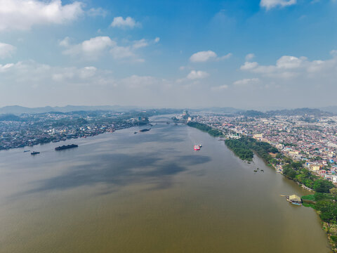 Aerial view of Mahakam River flowing through the city of Samarinda with cargo barges, urban buildings, and lush green vegetation in Samarinda, East Kalimantan, Indonesia.