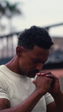 African American man bowing head with hands clasped near face in deep city street prayer