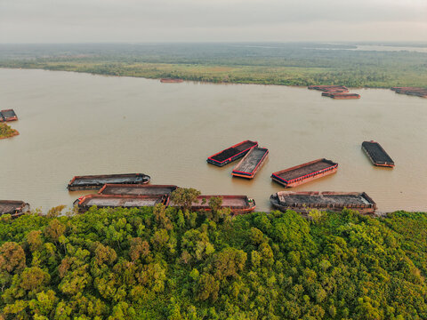 Aerial view of coal barges moored on the Mahakam river surrounded by dense tropical forest in Anggana, East Kalimantan, Indonesia.