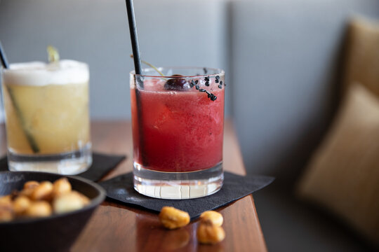 craft cocktail garnished with cherry on black napkin on wood table with fried corn kernels as snack in upscale bar