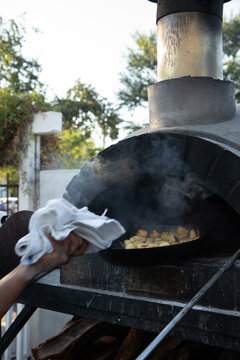 restaurant worker putting cast iron pan of vegetables into wood fired oven
