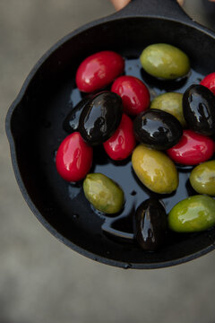 overhead shot of red, green, and black olives in oil in cast iron pan