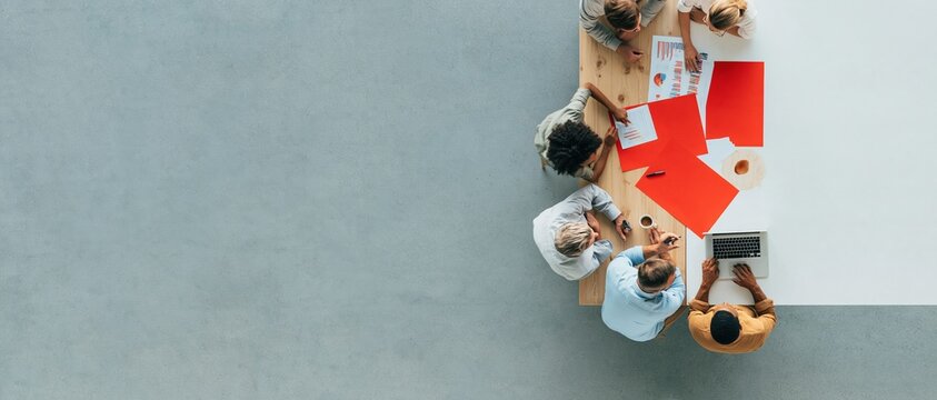 Business meeting with a diverse team planning over a wooden desk with red charts, featuring a clean surface and copy space for banners