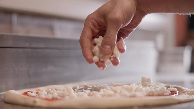 Slow motion hand sprinkling mozzarella cheese over pizza dough on kitchen countertop.