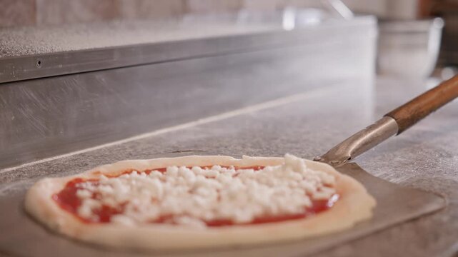 Tracking shot pizza being slid to metal peel from stone countertop in pizzeria prep area close lateral slow smooth movement following preparation.