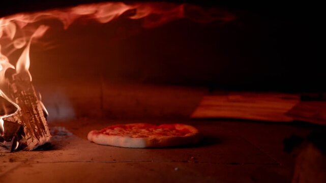 Slow motion pizza baking on stone oven floor with wood fired flames in hearth, static shot.