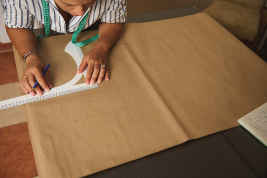 Woman drafting sewing pattern on kraft paper with measuring tape and ruler in a home studio