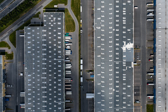 Aerial view of a large logistics warehouse facility with rows of trucks parked at loading docks and solar panels on the roof in Kunice, Central Bohemian Region, Czechia.