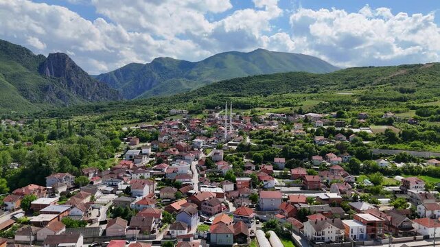 Aerial drone view of a traditional village with a prominent mosque surrounded by green mountains in North Macedonia.