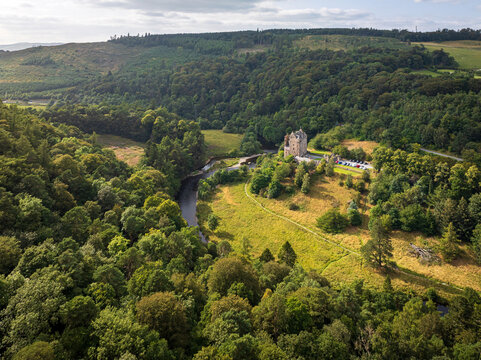 Aerial view of Neidpath Castle situated along the River Tweed, surrounded by dense forests, lush green meadows, and rolling hills in Peebles, Scotland, United Kingdom.