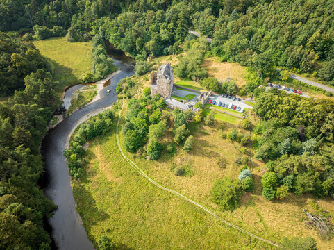 Aerial view of Neidpath Castle situated along the River Tweed, surrounded by lush green forests and rolling hills in Peebles, Scotland, United Kingdom.