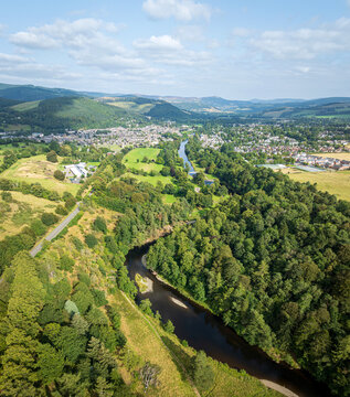 Aerial view of the River Tweed winding through lush green forests and rolling hills near the town of Peebles, Scotland, United Kingdom.