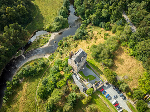 Aerial view of Neidpath Castle situated on the banks of the River Tweed, surrounded by lush green trees and meadows in Peebles, Scotland, United Kingdom.