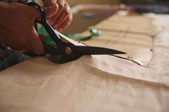 Woman cutting fabric with large scissors following a paper pattern in a sewing studio