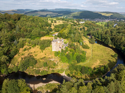 Aerial view of Neidpath Castle situated on a grassy hill overlooking the River Tweed, surrounded by lush green forests and rolling hills in Peebles, Scotland, United Kingdom.