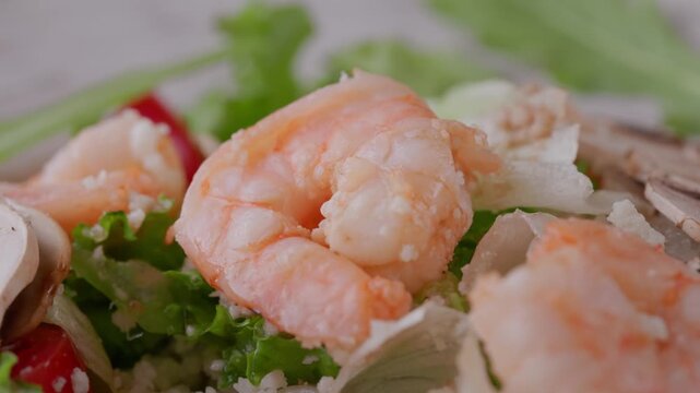 Tracking shot of shrimp and prawn on mixed salad with mushrooms and lettuce on plate in kitchen.