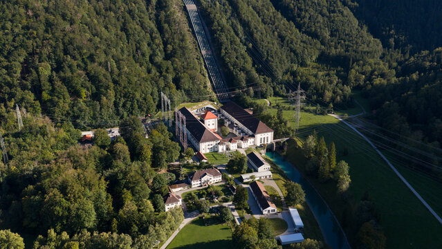 Aerial view of Walchenseekraftwerk hydroelectric power plant with its prominent penstock pipeline, turquoise water canal, and surrounding lush forest in Kochel am See, Bayern, Germany.
