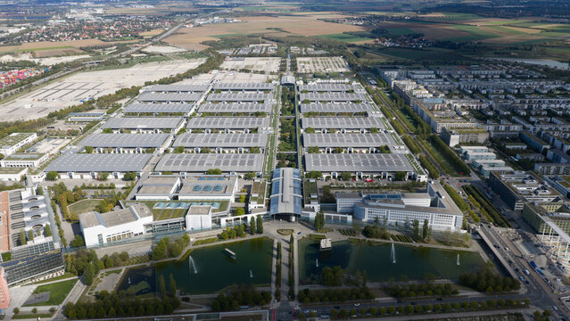 Aerial view of Messe Munchen exhibition center with its large flat rooftops, surrounding green spaces, and water features in Munchen, Bayern, Germany.