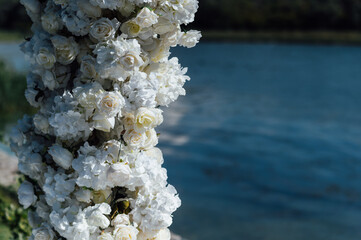 Obraz premium White rose floral arch detail for outdoor wedding ceremony by the lake.