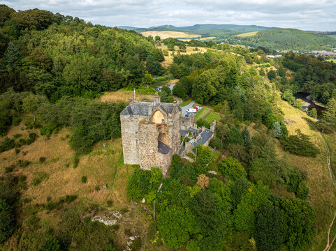 Aerial view of Neidpath Castle surrounded by lush green trees and rolling hills in Peebles, Scotland, United Kingdom.