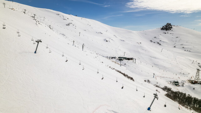 Aerial view of Cerro Catedral ski resort with chairlifts traversing snow-covered slopes under a clear blue sky in Bariloche Department, Rio Negro Province, Argentina.