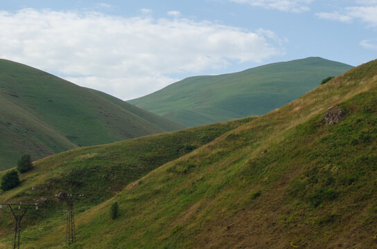 Close-up view of lush green rolling hills and mountain slopes under a bright cloudy sky.   