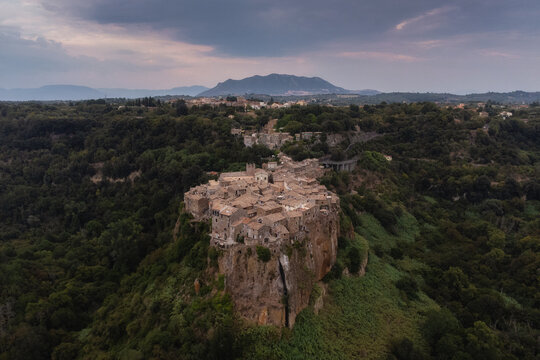 Aerial view of the historic hilltop village of Calcata Vecchia perched on a volcanic cliff surrounded by lush forests and dramatic cloudy skies in Calcata Vecchia, Lazio, Italy.
