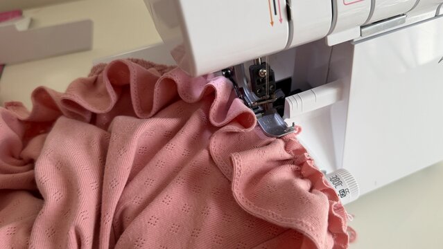 Aesthetic sewing workspace with an overlock machine, serger, fabric, threads and sewing accessories. Cozy atmosphere, the art of sewing, handmade fashion and garment making in a bright sewing studio
