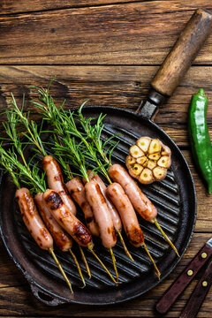 Grilled sausages on rosemary skewers on grill iron pan. Wooden background