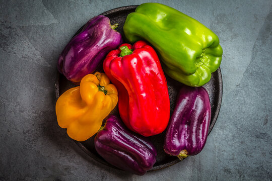Many colored bell peppers on black plate, grey slate background