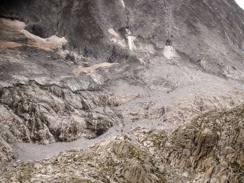 Aerial view of Presanella mountain range with rugged rocky slopes, glacial remnants, and a small hiker in a red jacket standing on the terrain in Giustino, Trentino-Alto Adige, Italy.